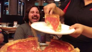 man laughing while cheesy pizza is being served